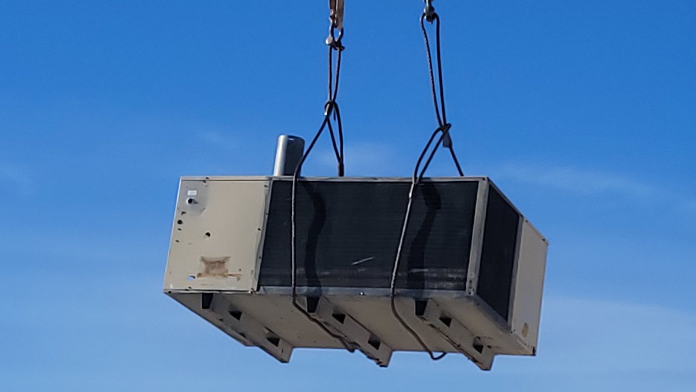 Commercial HVAC unit being hoisted by crane during installation